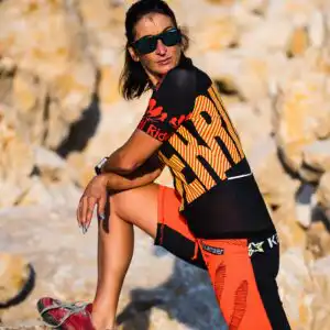 Auffälliges Damen Fahrradtrikot Rider in Schwarz Rot Gelb mit rotem Splash Print am Ärmel, getragen in einer ockerfarbenen Felsenlandschaft mit orangefarbener Baggy Shorts