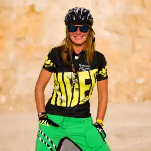Stylisches Damen MTB Trikot kurzarm Flow Rider in Schwarz mit gelben Blumenarmeln und Rider-Schriftzug in einer felsigen Landschaft