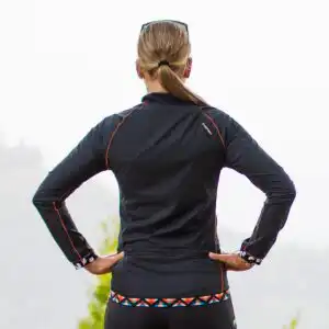 Rückansicht der Killertaler Damen Radwindjacke Etna in Schwarz mit orangen Ziernähten, buntem Ethno-Abschlussstreifen und optionaler Rückentasche mit Reißverschluss.