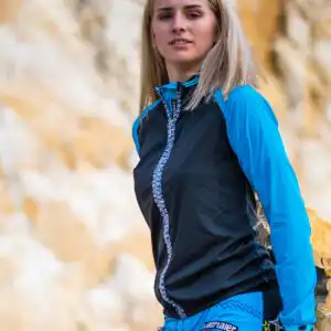 Seitenansicht der Damen Radwindjacke Tramontana in Türkis-Schwarz. Zeigt die taillierte Maßpassform und den Übergang zur Rider Bike Shorts.