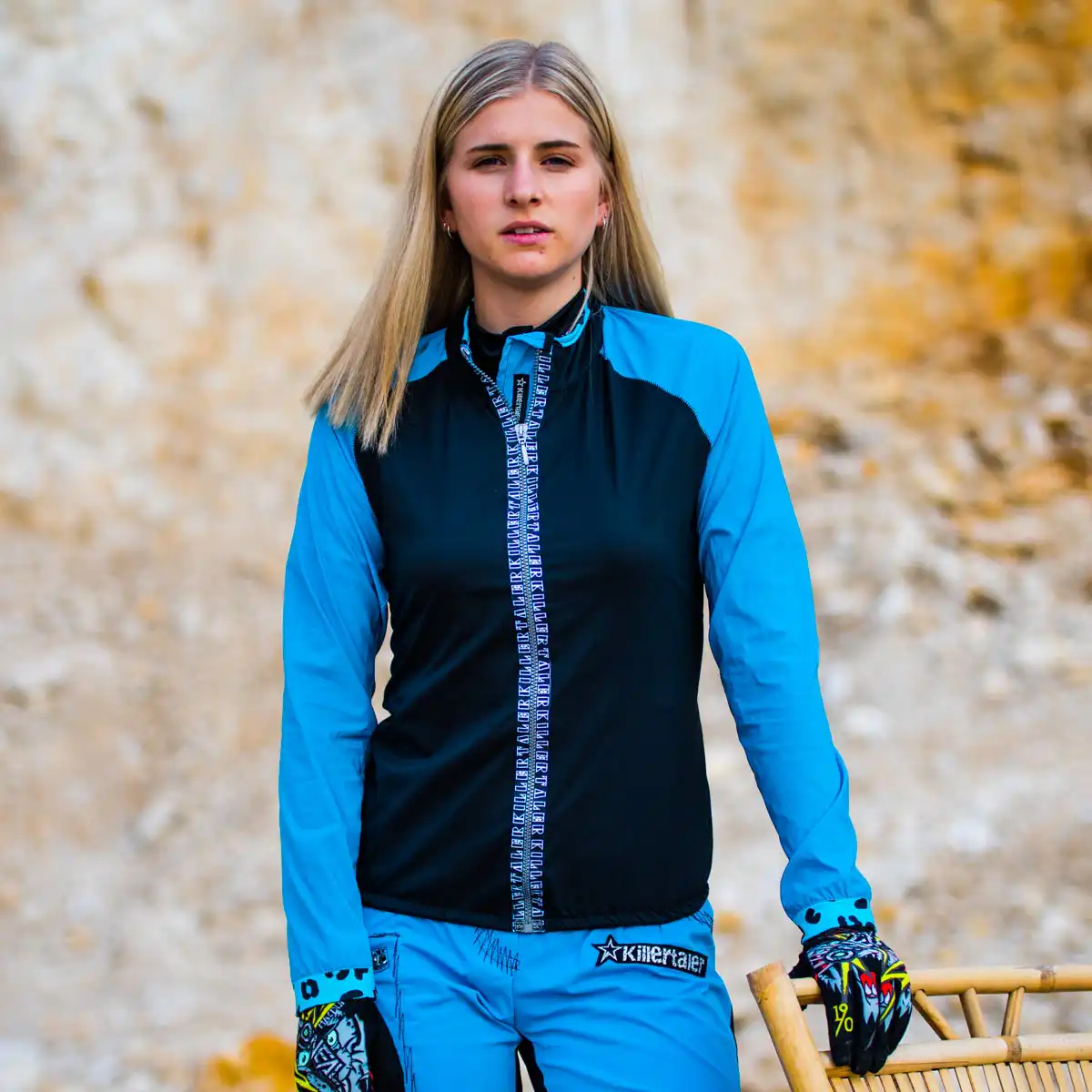 Zweifarbige Killertaler Damen Fahrrad Windjacke Tramontana in Türkis-Schwarz mit elastischem Stretch und blau-schwarzer Rider Bike Shorts in felsiger Landschaft.